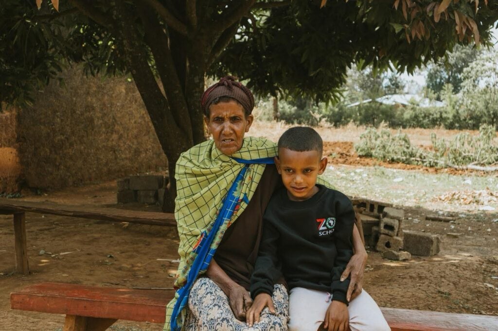Elderly woman with young boy sitting outdoors under a tree, representing community support by The Zoe Project.