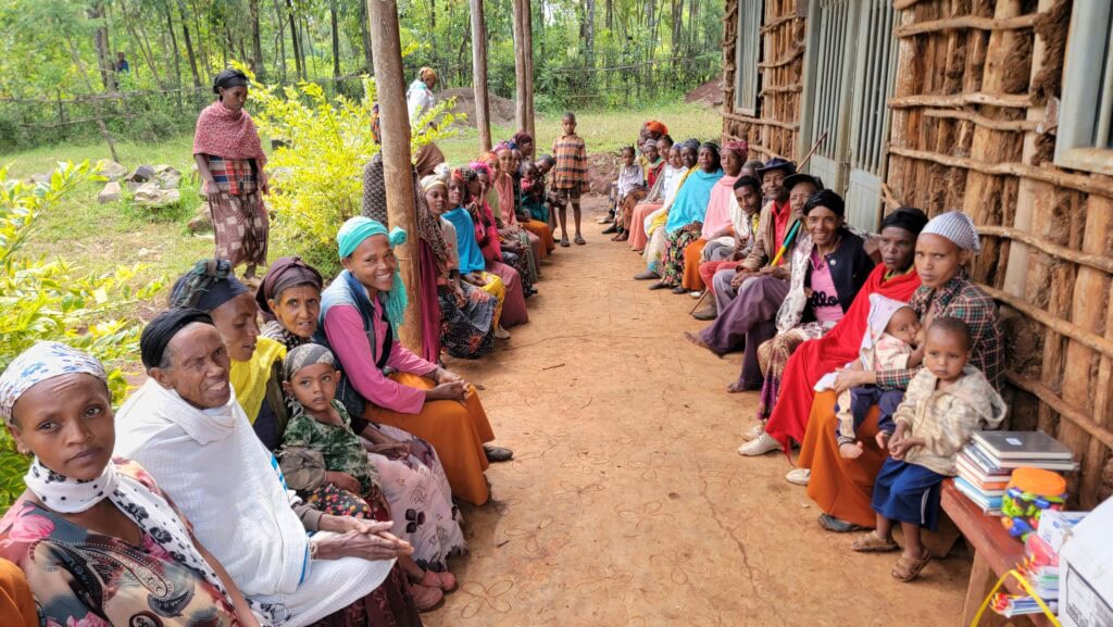 Women and children gathered outside a traditional Ethiopian hut for community meeting, promoting education and empowerment.