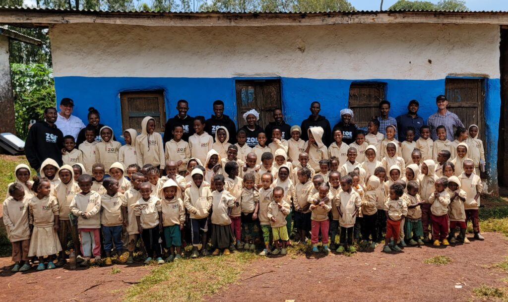 Children with school uniforms and staff outside a blue rural school building in Ethiopia.
